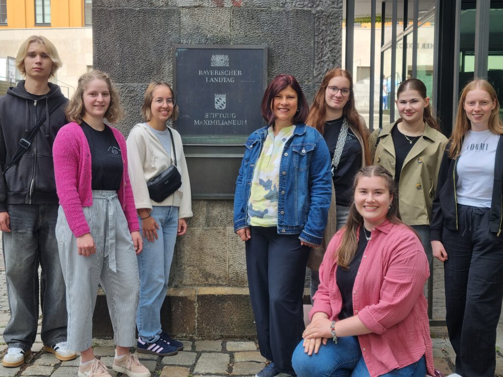 Schüler der 11. Klasse stehen gemeinsam mit ihrer Lehrerin um das Schild "Bayerischer Landtag" herum