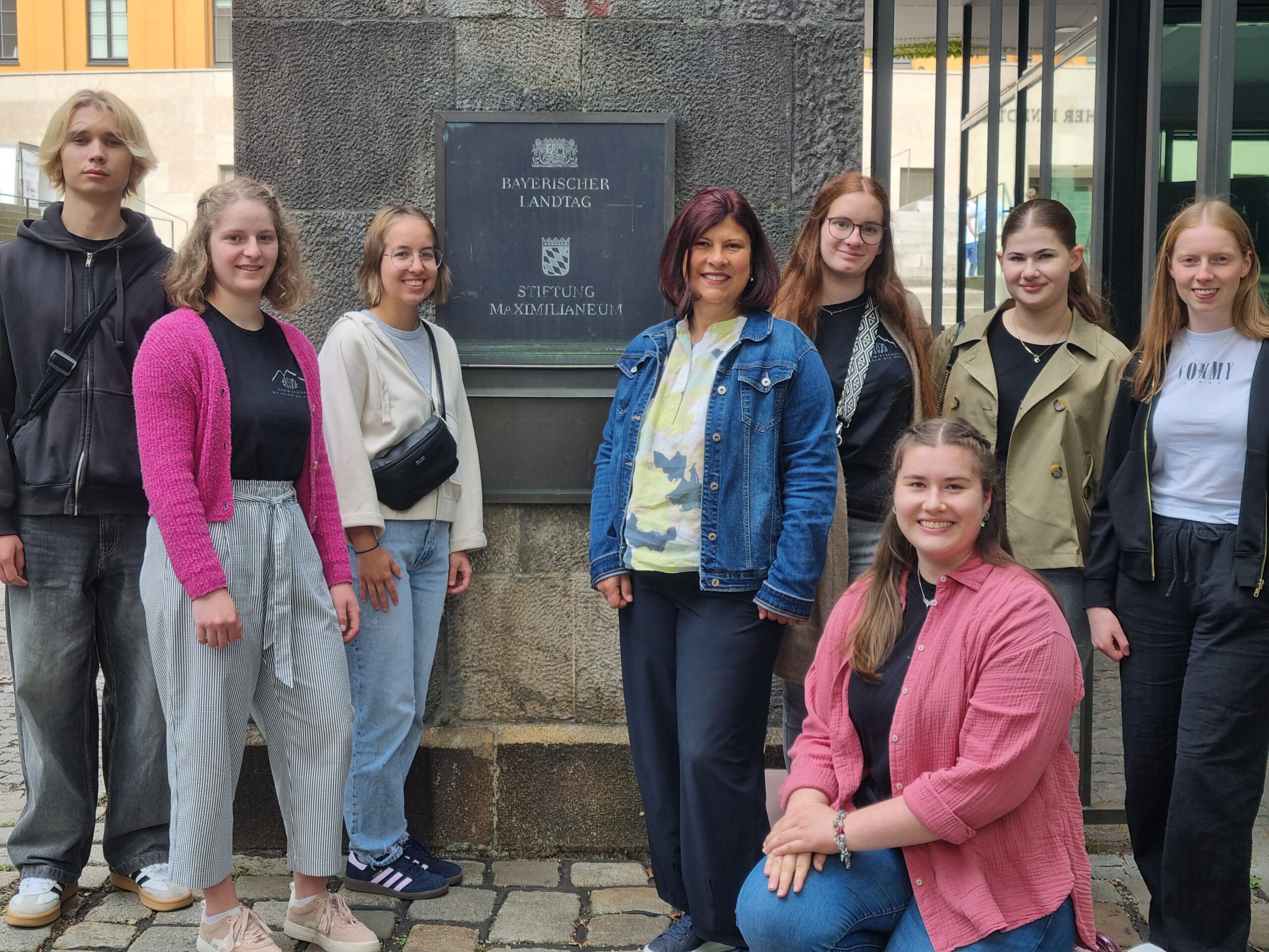 Schüler der 11. Klasse stehen gemeinsam mit ihrer Lehrerin um das Schild "Bayerischer Landtag" herum