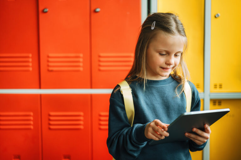 Schul-Mädchen mit Tablet in der Hand vor Spint-Schränken, vermutlich in einer Schule