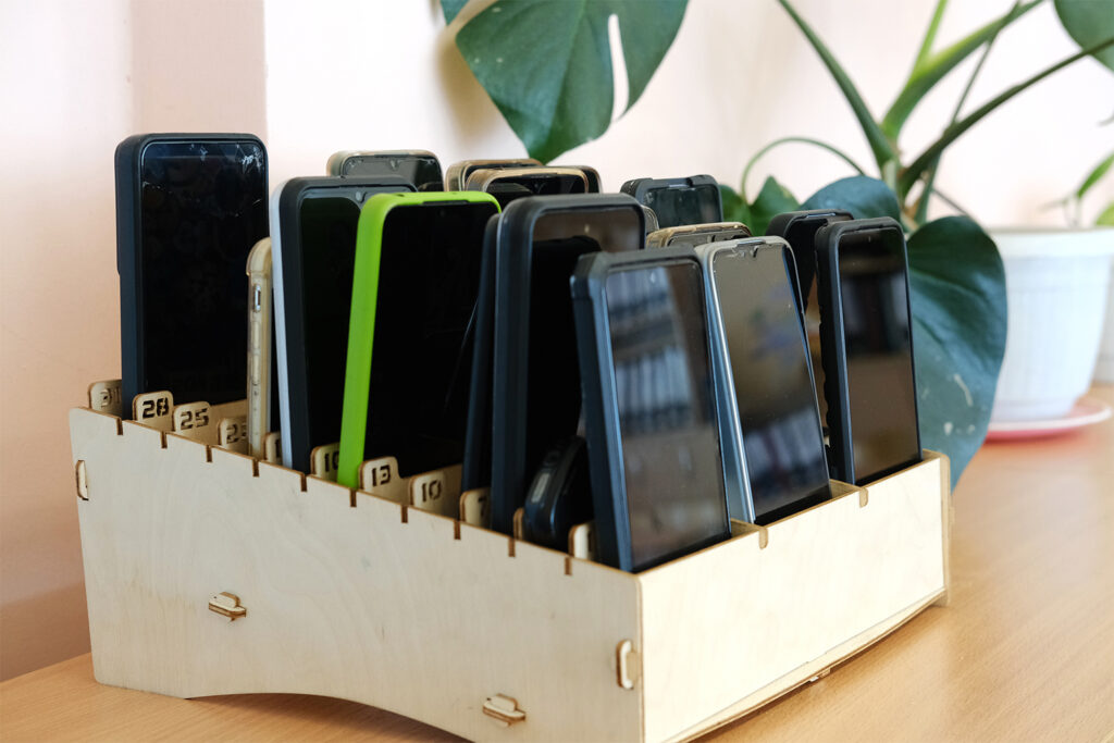 Mobiltelefone von Schulkindern, die in einer Holzkiste auf einem Klassenzimmer aufbewahrt werden, was das Verbot von Ger&auml;ten w&auml;hrend Bildungsaktivit&auml;ten veranschaulicht und den Fokus auf das Lernen f&ouml;rdert